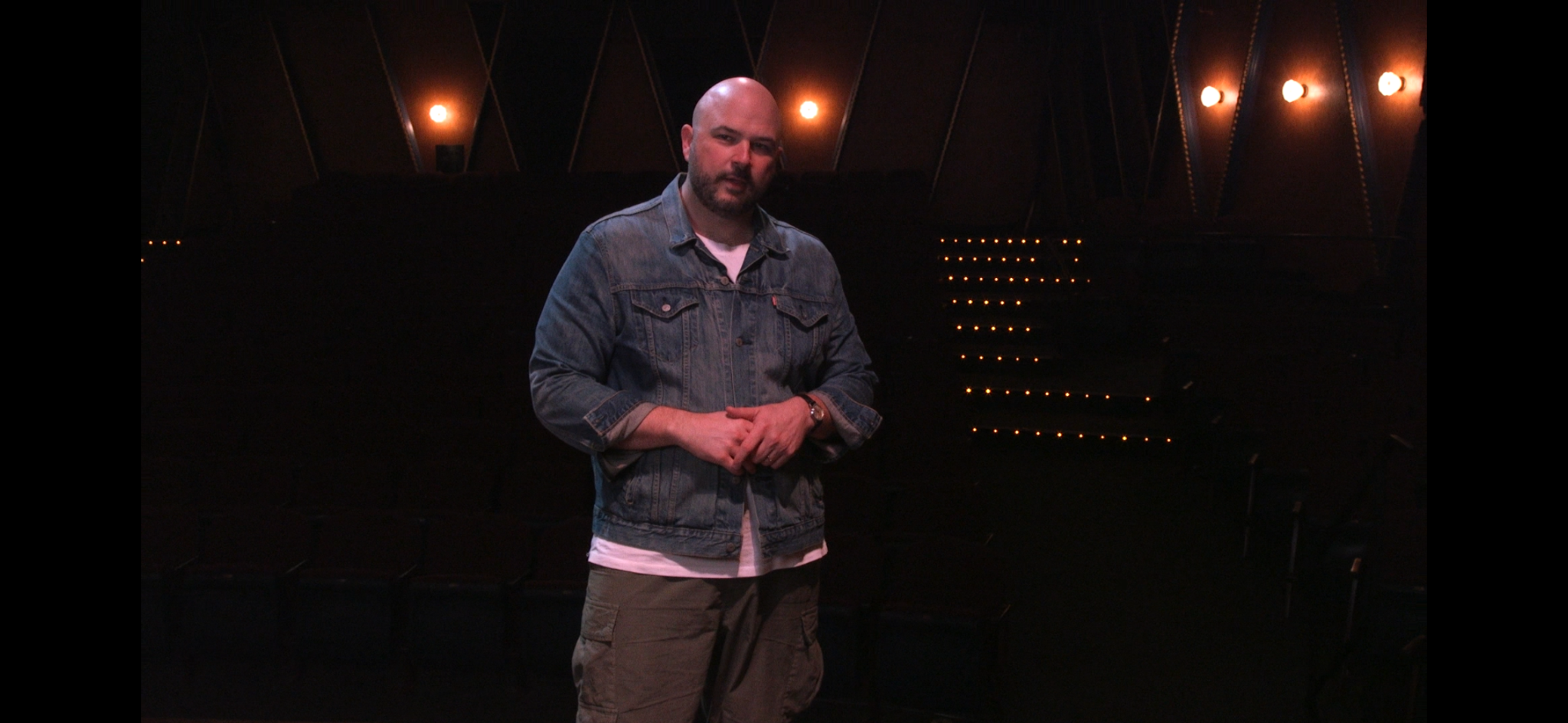 Taylor Harris in a denim jacket on a dark stage with warm lights